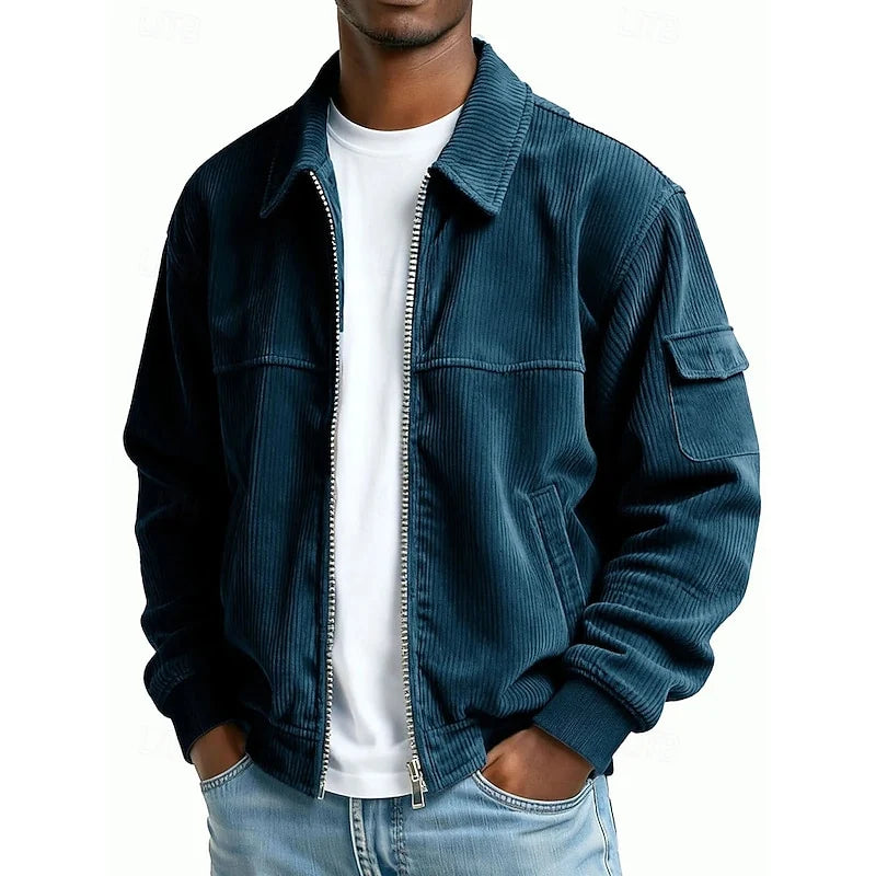 A man wearing a dark blue corduroy zip-up jacket over a white t-shirt and light blue jeans, shown from the chin down against a plain white background.