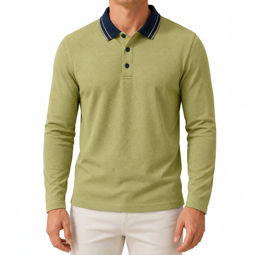 A man wearing a light olive green long-sleeve polo shirt with a navy blue collar and white piping, paired with white pants, in a bright, modern indoor setting.