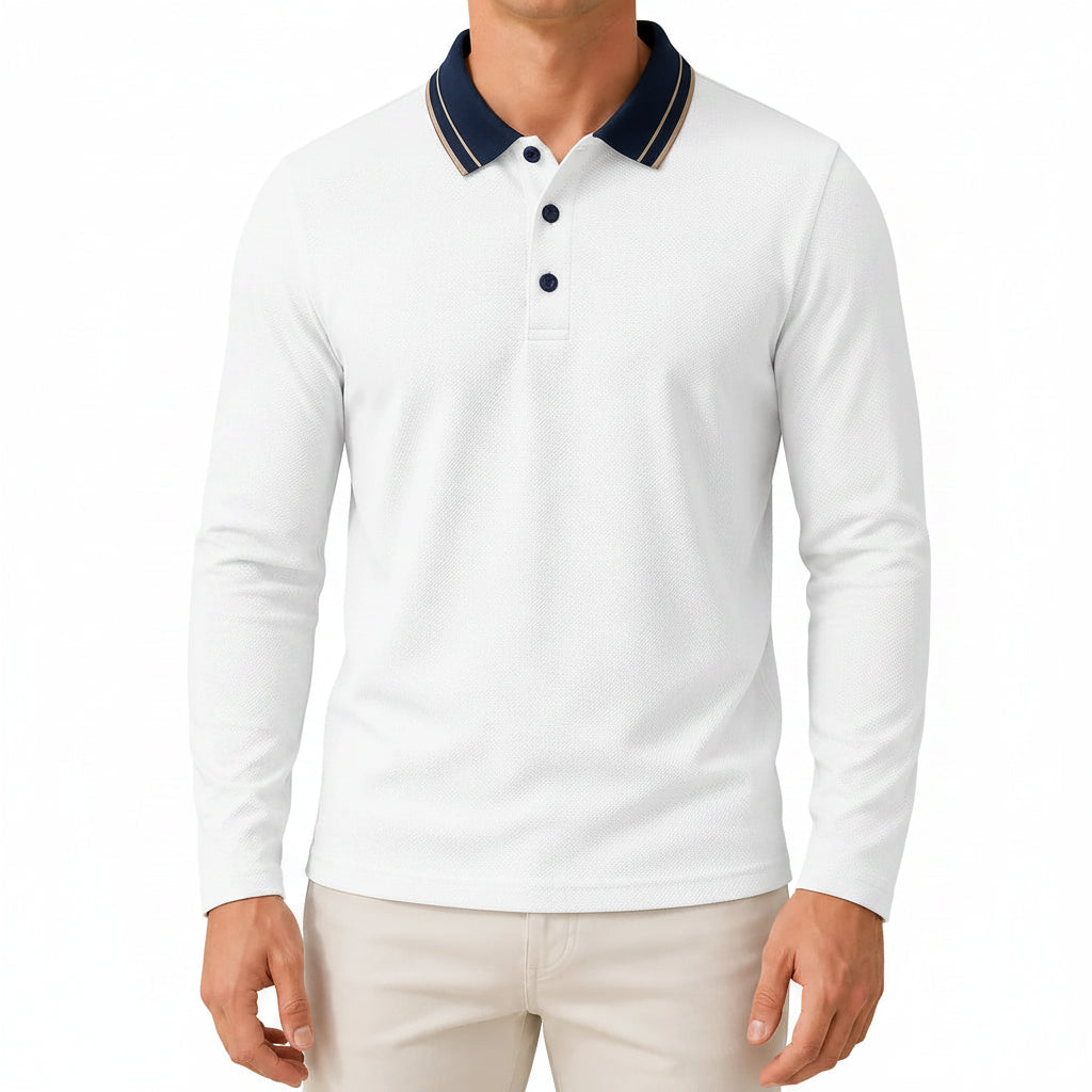 A man wearing a light olive green long-sleeve polo shirt with a navy blue collar and white piping, paired with white pants, in a bright, modern indoor setting.