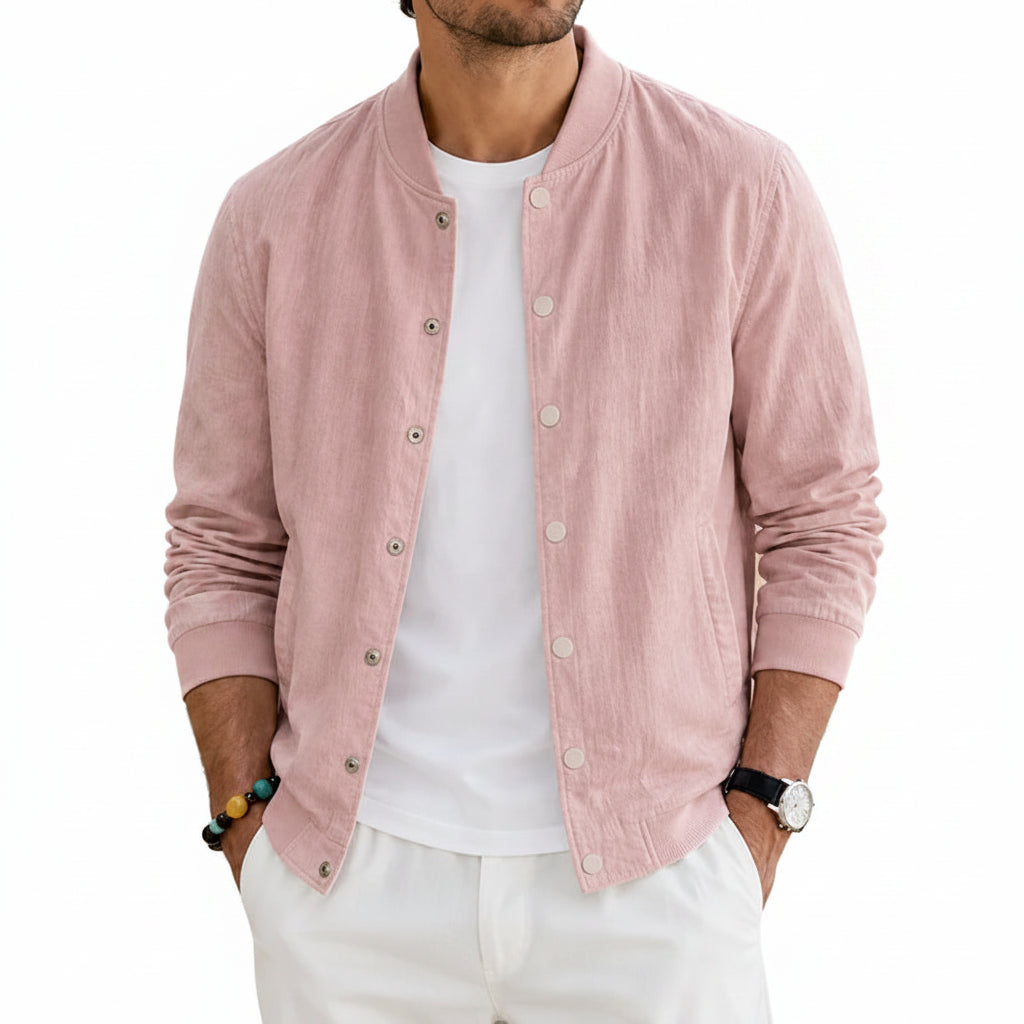A man wearing a light blue button-up linen-blend jacket over a white t-shirt and white pants, standing in a sunlit outdoor patio setting.