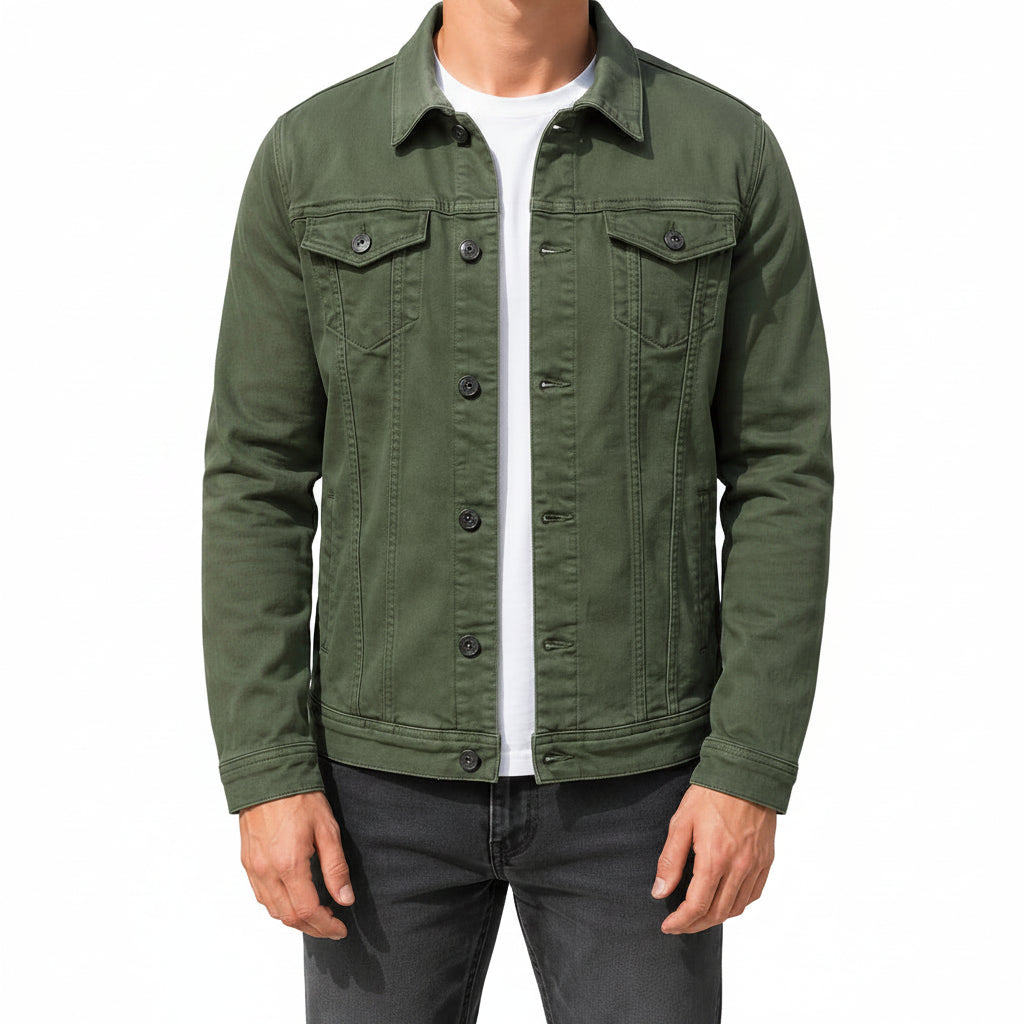 A man wearing an olive green canvas utility jacket over a white t-shirt and dark gray jeans, standing outdoors against a concrete wall.