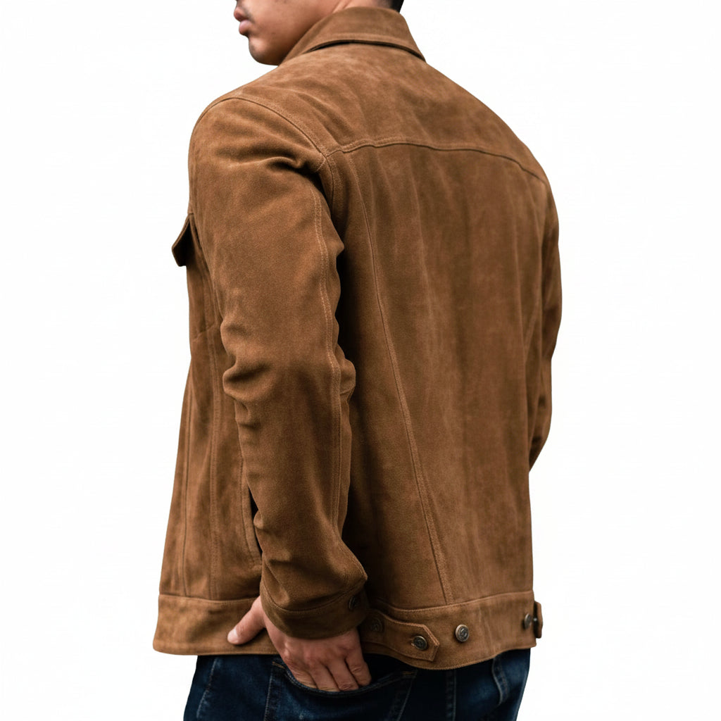 A man wearing a brown suede button-up jacket over a gray t-shirt and blue jeans, standing in front of a rustic wooden log wall.